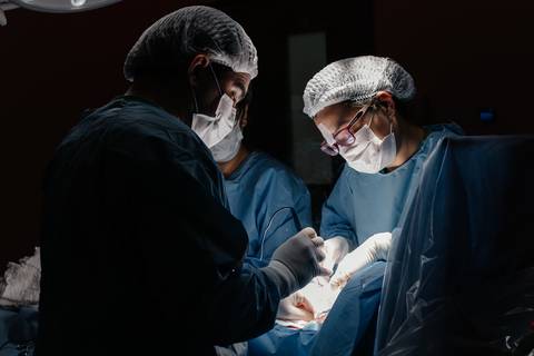 Equipe médica focada realizando o parto sob iluminação cirúrgica.'