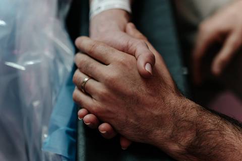 Plano detalhe das mãos do casal seguradas com força e carinho.'