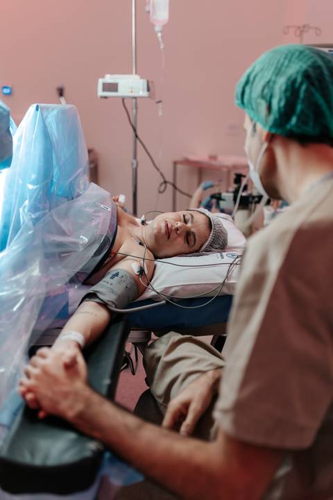 Visão ampla da sala de cirurgia com a mãe deitada aguardando o nascimento.'