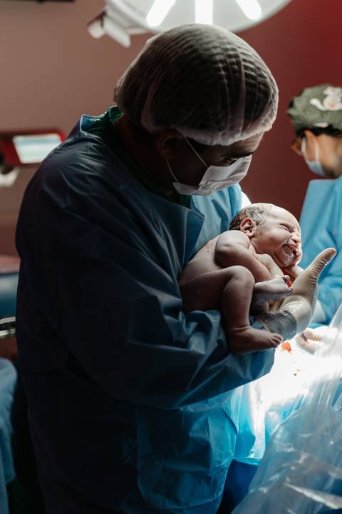 Médico obstetra segurando o bebê recém-nascido no momento do nascimento.'