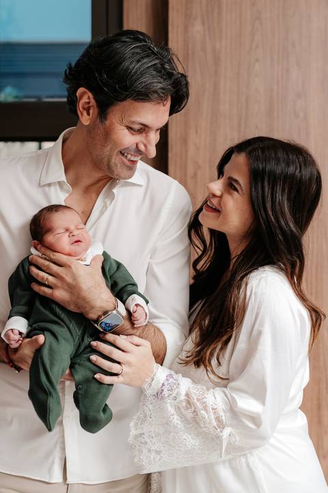 Casal no quarto de maternidade admirando o filho Enrico no colo do pai.'
