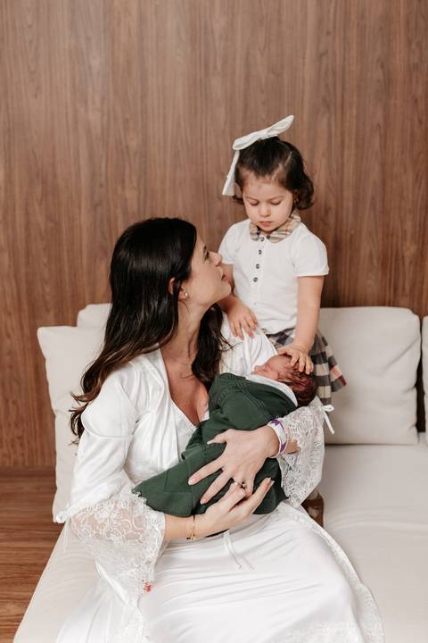 Mãe com o bebê no colo conversando e sorrindo para a filha mais velha.'