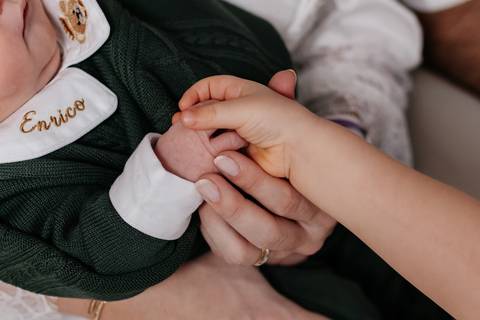 Mãozinha da irmã mais velha segurando a mão do bebê Enrico.'