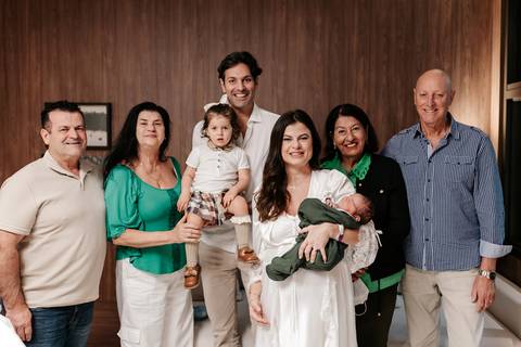 Foto em grupo com avós e família reunidos no quarto de maternidade.'