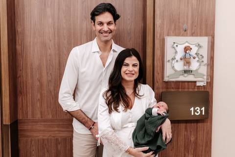Casal posando na porta do quarto 131 ao lado do enfeite de maternidade.'