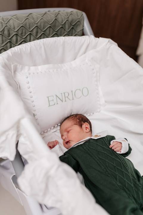 Bebê Enrico dormindo tranquilo ao lado da almofada bordada com seu nome.'