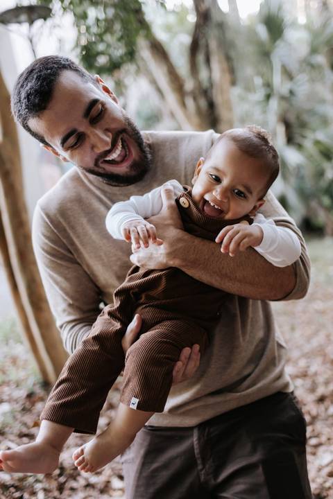 Matheus segurando Rafael no colo durante ensaio de família ao ar livre'