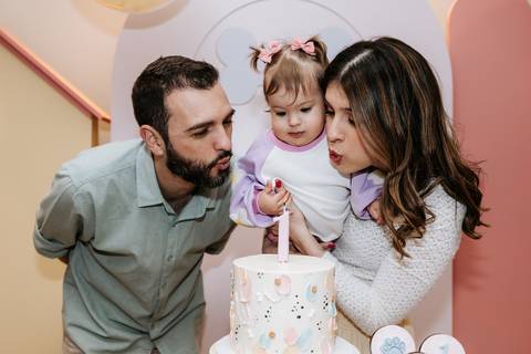 Olívia entre os pais diante do bolo de aniversário, durante a comemoração de 1 ano.'