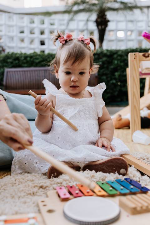 Olívia segurando uma baqueta enquanto participa de uma brincadeira musical durante sua festa de 1 ano.'