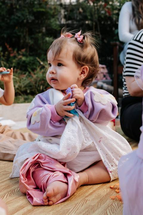 Olívia sentada no chão, segurando um brinquedo colorido durante a comemoração.'