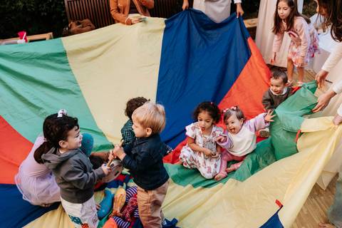 Crianças brincando juntas em um espaço com tecido colorido durante a festa.'