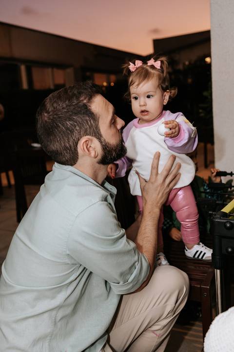 Pai segurando Olívia no colo durante a comemoração de seu primeiro aniversário.'