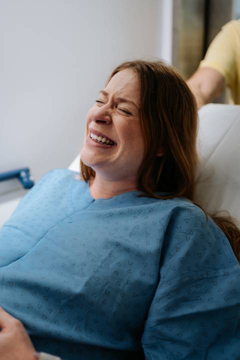 Jessica sorri emocionada durante o trabalho de parto, deitada na cama da maternidade.'