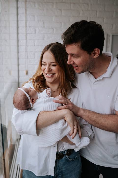 Jessica e Fabrício seguram Maria Clara nos braços e trocam sorrisos enquanto contemplam a filha nos primeiros dias de vida.'