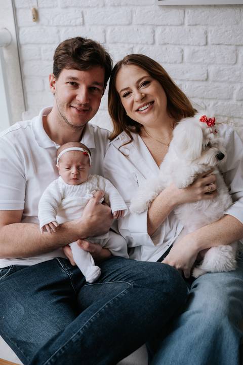 Jessica e Fabrício posam com Maria Clara nos braços ao lado da cachorrinha da família, registrando os primeiros dias da bebê em casa.'