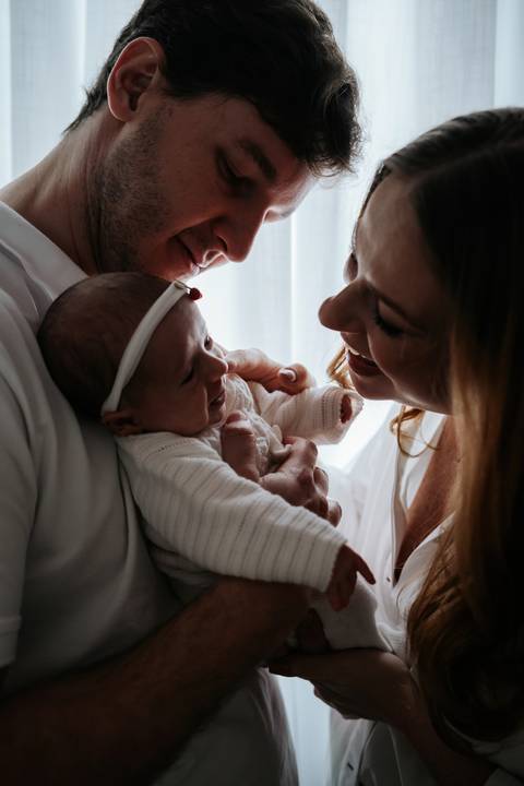 Jessica e Fabrício observam Maria Clara de pertinho, trocando olhares carinhosos com a filha durante os primeiros dias em casa.'
