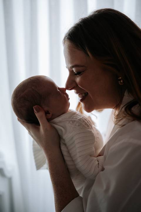 Jessica segura Maria Clara pertinho do rosto e sorri ao contemplar a filha, em um momento de carinho e conexão entre mãe e bebê.'