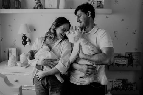 Foto em preto e branco do casal sorrindo no quarto com Maria Clara e o gato de estimação.'