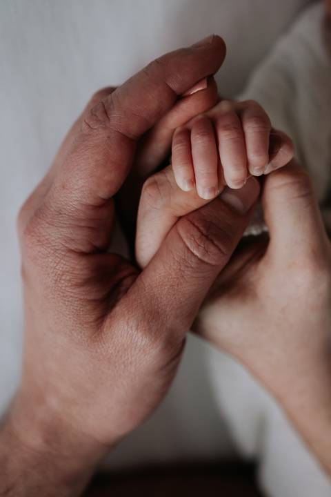 Plano detalhe das mãozinhas de Maria Clara segurando as mãos dos pais.'