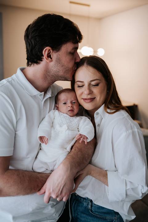 Jessica e Fabricio abraçados com a bebê Maria Clara acordada em seus braços.'