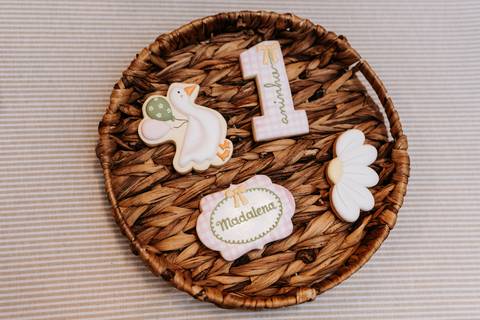 Docinhos personalizados com gansinhos, laços e o nome Madalena, compondo a decoração da festa.'