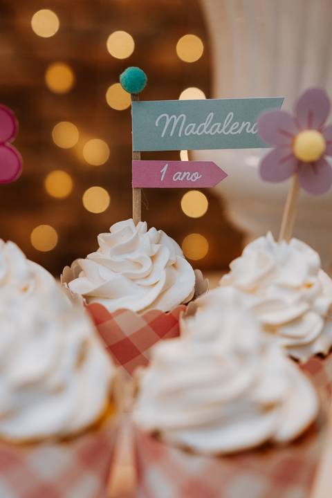 Cupcakes decorados com chantilly e plaquinha de 1 ano, celebrando o aniversário da Madalena.'