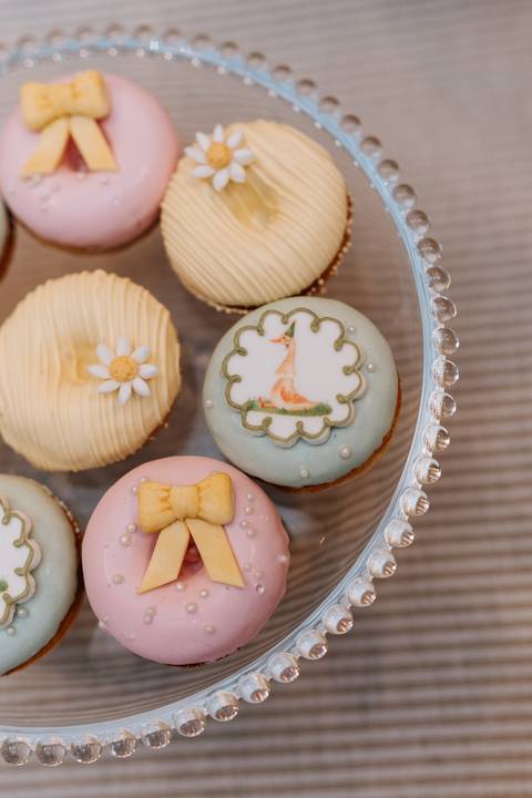 Biscoitos decorados com flores, laços e gansinhos, seguindo a delicada paleta de cores da comemoração.'