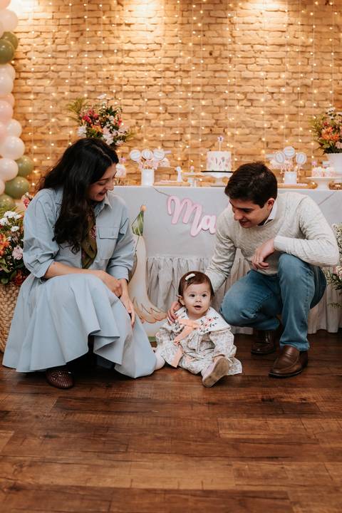 Madalena aparece sentada entre a mamãe Mariana e o papai Pedro Henrique, em um registro especial diante da mesa decorada.'