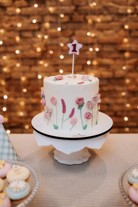 Close do bolo de Madalena, com flores em relevo e acabamento delicado em tons suaves.'