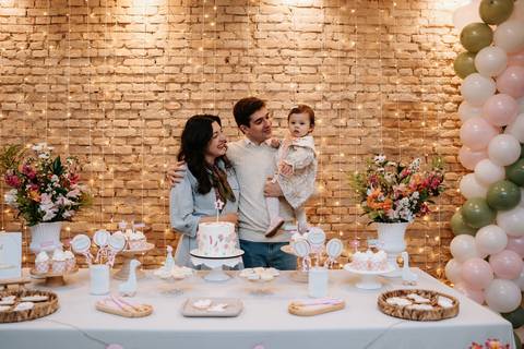 Mariana e Pedro Henrique seguram Madalena diante da mesa principal, celebrando juntos esse marco tão especial.'