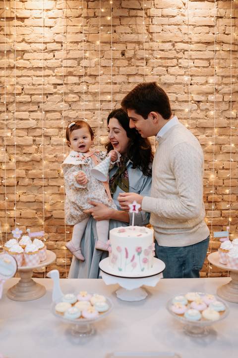 A família se reúne ao redor do bolo para comemorar o primeiro aniversário da Madalena, em um momento repleto de amor e alegria.'