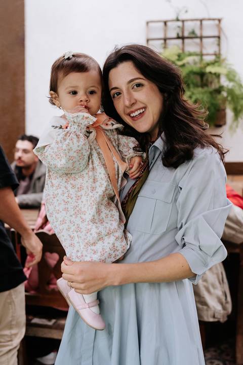 Mariana segura Madalena no colo em um momento de carinho e cumplicidade durante a comemoração.'