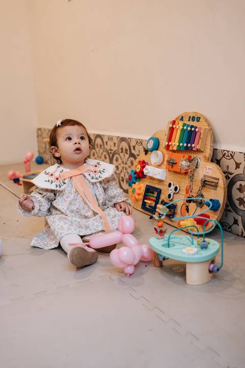 Madalena se diverte no cantinho de brinquedos, explorando instrumentos musicais e atividades preparadas para a comemoração.'