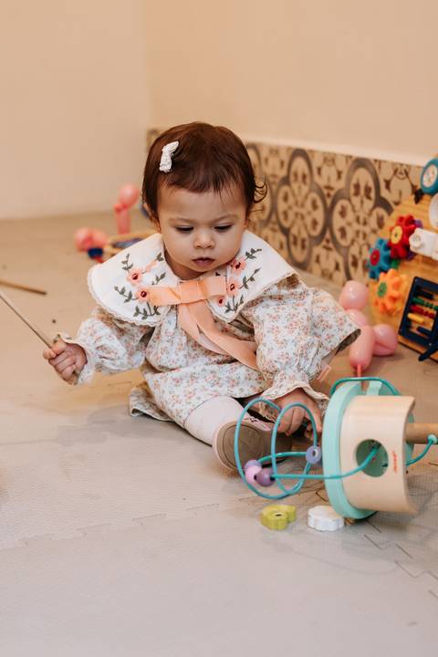 Madalena se diverte no cantinho de brinquedos, explorando instrumentos musicais e atividades preparadas para a comemoração.'