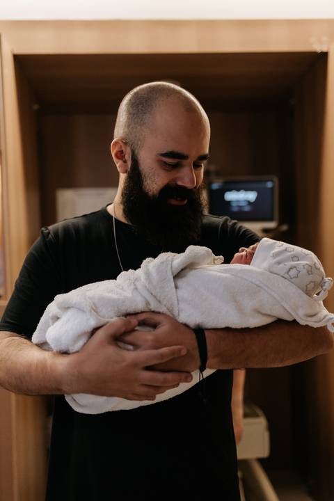 Papai Bruno segura Julieta nos braços pela primeira vez, com carinho e emoção.'