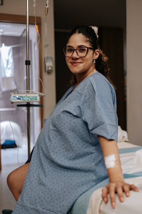 Yasmin posa ao lado da cama da maternidade, registrando os momentos que antecedem a chegada da filha.'
