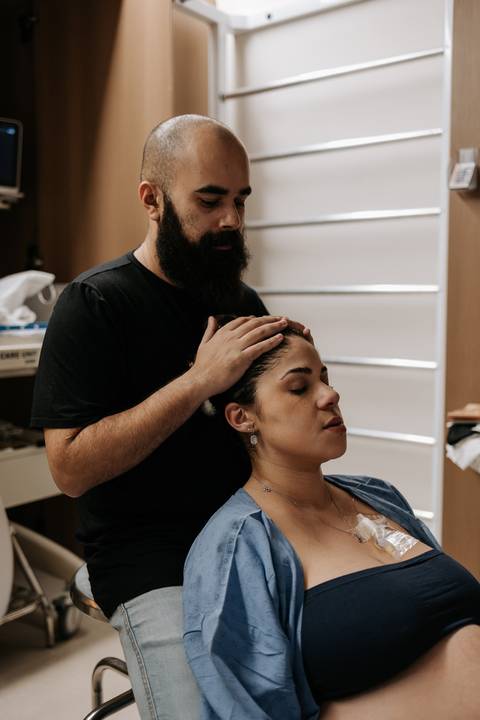 Bruno massageia delicadamente a cabeça de Yasmin, oferecendo conforto e apoio durante o trabalho de parto.'