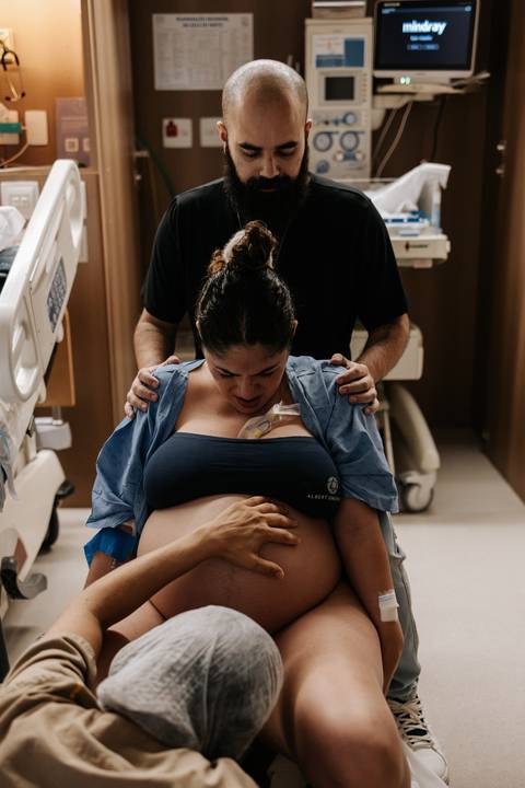 Bruno apoia os ombros de Yasmin enquanto ela respira e se concentra durante o trabalho de parto.'