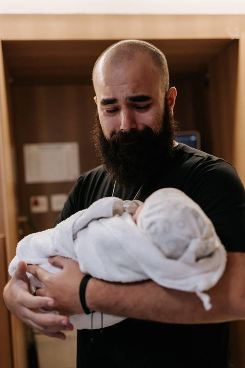 Papai Bruno segura Julieta enrolada na manta e observa a filha com ternura.'