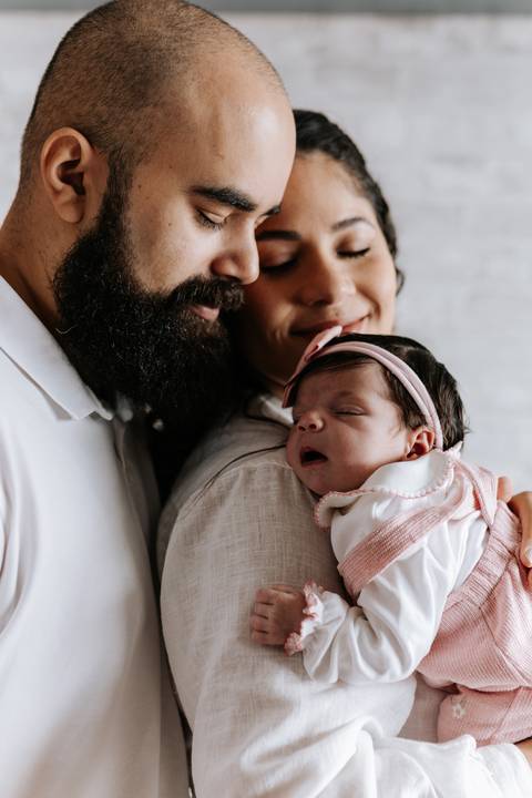 Papai beijando Julieta enquanto ela descansa no colo da mamãe.'
