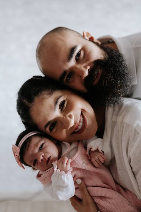 Retrato de Julieta aconchegada entre os pais, com sorrisos e carinho.'