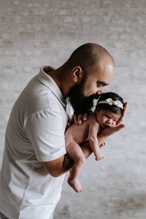 Papai Bruno segurando Julieta com delicadeza e dando um beijo carinhoso na filha.'