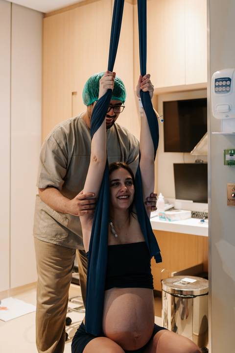 Ana Carolina utilizando o tecido de apoio durante o trabalho de parto, com o suporte e carinho de Samuel.'