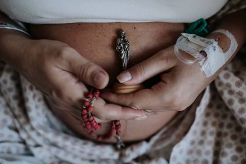 Mãos de Marina e José Carlos unidas segurando o crucifixo do terço sobre o ventre.'
