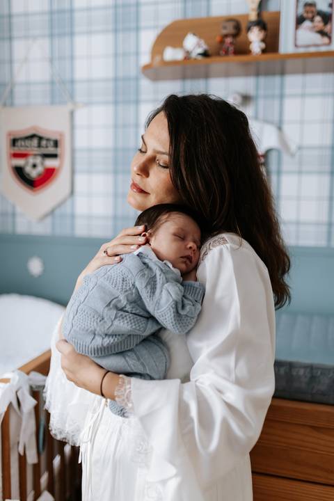 Marina com José Joaquim adormecido em seu ombro no quarto com tema de futebol.'