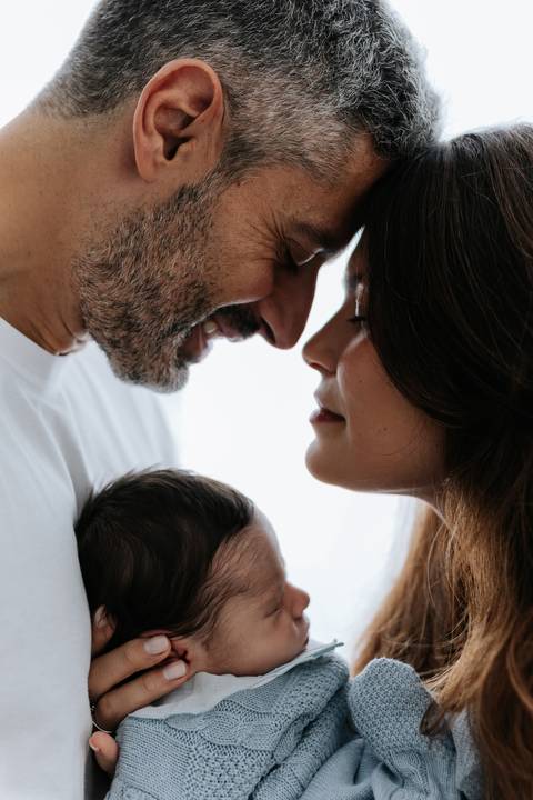 Close intimista do casal encostando as testas com carinho sobre a cabecinha do bebê.'
