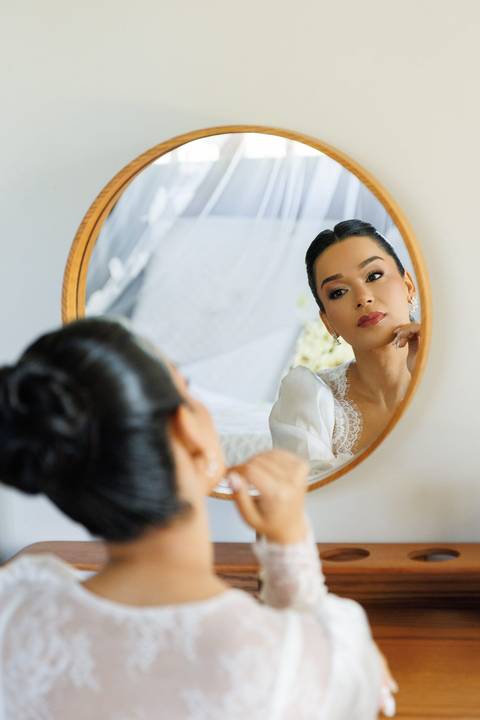 Noiva diante do espelho durante o making of, vivendo a emoção dos preparativos antes do casamento.'
