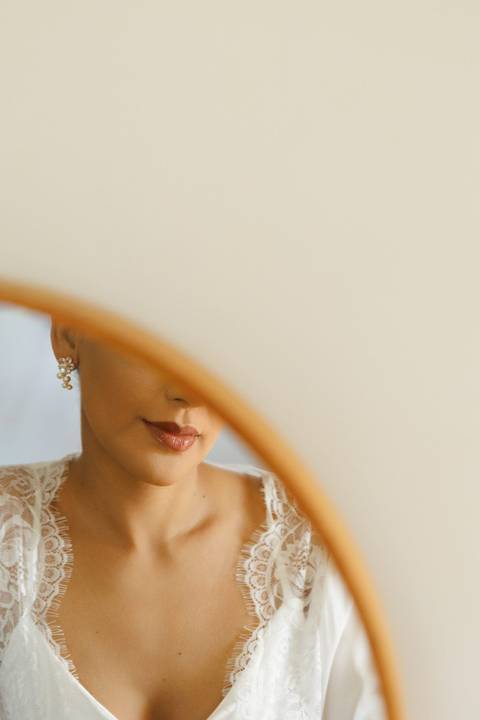 Noiva diante do espelho durante o making of, vivendo a emoção dos preparativos antes do casamento.'