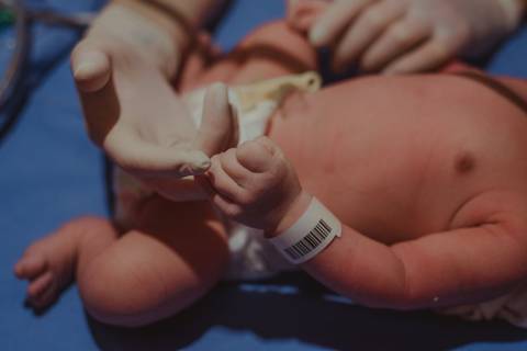 bebê com pulseira de identificação segurando mão de pediatra'