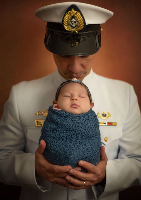 bebê nas mãos do pai vestido com traje oficial da Marinha'
